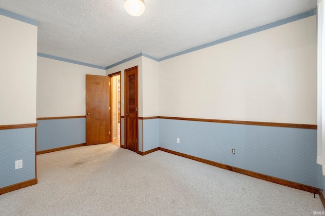 carpeted empty room with baseboards, a textured ceiling, and wallpapered walls