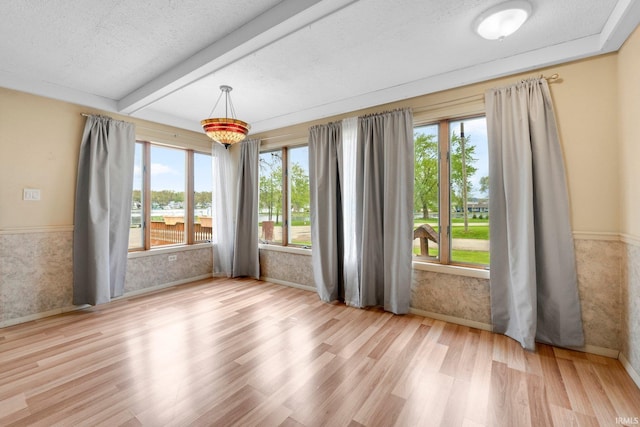 unfurnished room featuring healthy amount of natural light, wood finished floors, beam ceiling, baseboards, and a textured ceiling