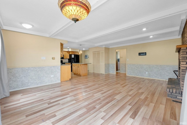 unfurnished living room with light wood finished floors, a wainscoted wall, beam ceiling, a fireplace with raised hearth, and recessed lighting