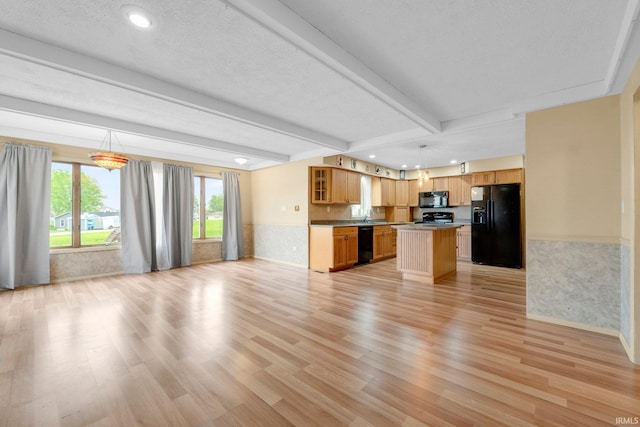 kitchen featuring black appliances, open floor plan, light wood-style flooring, a center island, and beamed ceiling