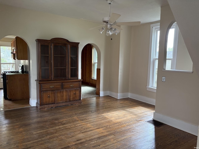 unfurnished dining area featuring ceiling fan, dark wood finished floors, baseboards, and arched walkways