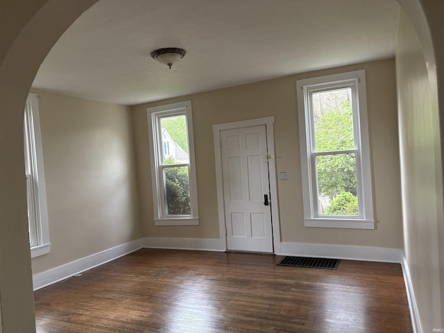 foyer with arched walkways, dark wood finished floors, and baseboards