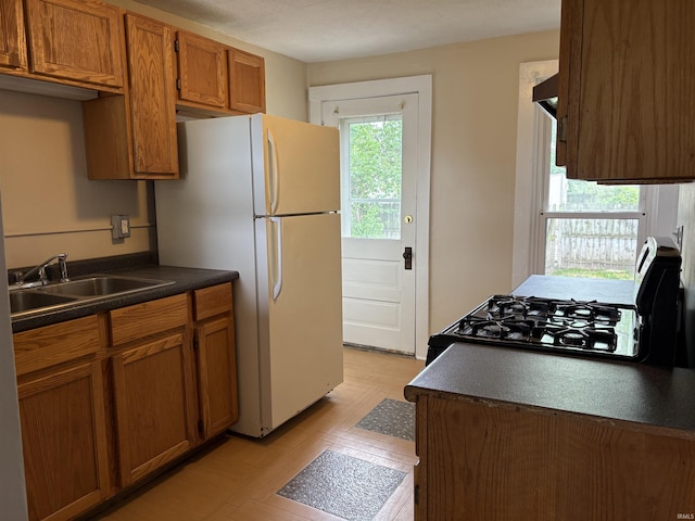 kitchen with a sink, dark countertops, brown cabinets, freestanding refrigerator, and black range with gas cooktop