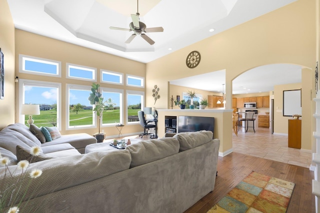 3090 Kellygreen Dr, Angola, IN 46703 - living room featuring arched walkways, a ceiling fan, a high ceiling, light wood-type flooring, and a tray ceiling
