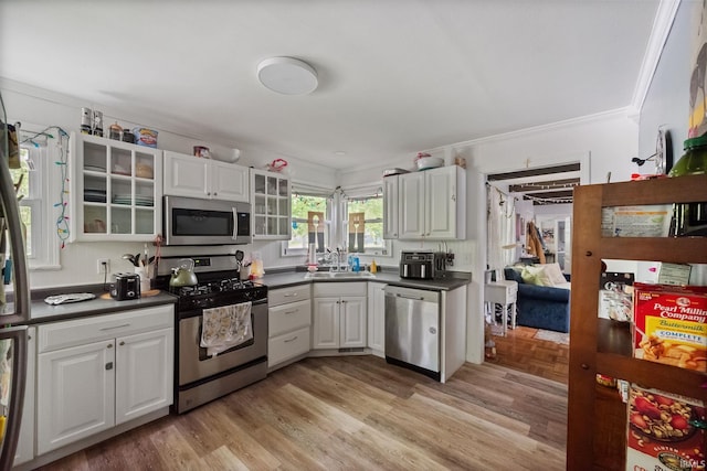 kitchen with stainless steel appliances, a sink, dark countertops, crown molding, and glass insert cabinets
