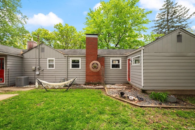 back of property with a chimney, cooling unit, a yard, and a shingled roof