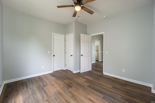 unfurnished bedroom with dark wood-style flooring, baseboards, freestanding refrigerator, and a ceiling fan