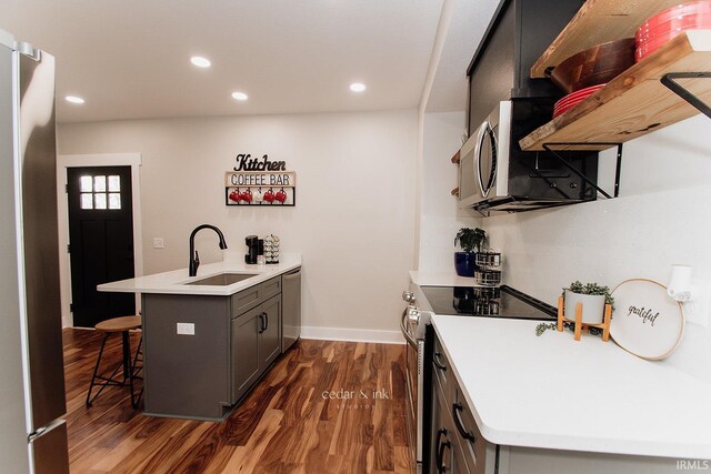 kitchen with a sink, a peninsula, stainless steel appliances, a breakfast bar, and dark wood-type flooring