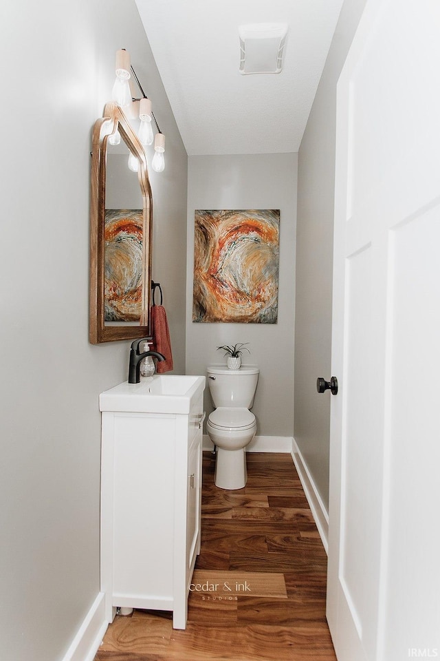 half bathroom with wood finished floors, toilet, vanity, and baseboards