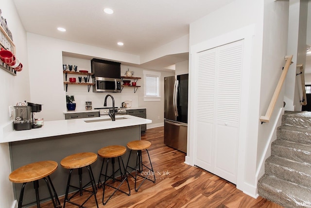 kitchen featuring stainless steel appliances, open shelves, a peninsula, wood finished floors, and a breakfast bar area
