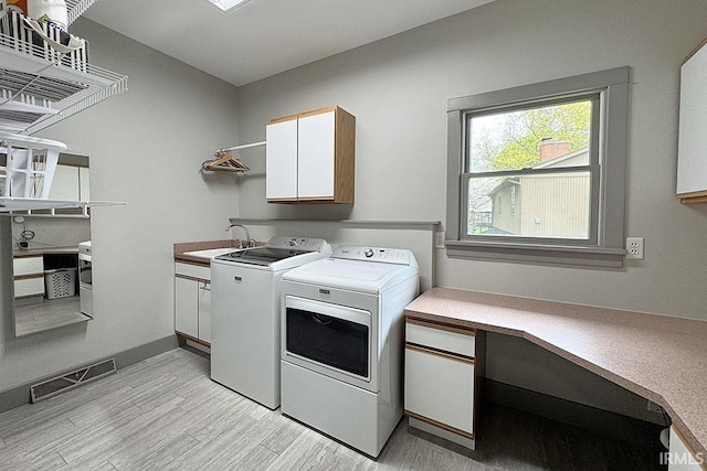 laundry area featuring cabinet space, washing machine and clothes dryer, and light wood finished floors