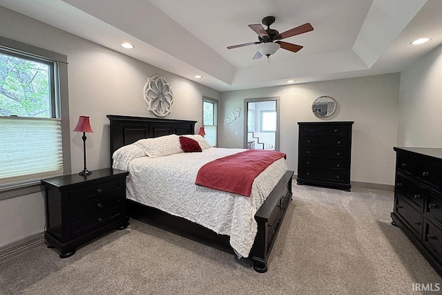 bedroom featuring light carpet, a raised ceiling, recessed lighting, baseboards, and ceiling fan