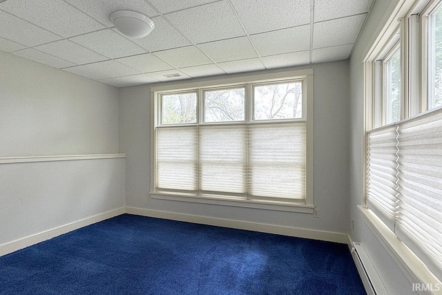 spare room with dark colored carpet, plenty of natural light, a paneled ceiling, baseboard heating, and baseboards