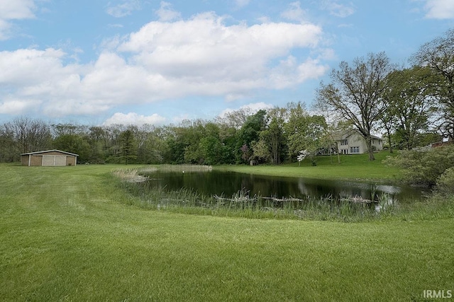 view of grassy yard featuring a water view, a detached garage, and a forest view