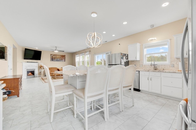 dining area with healthy amount of natural light, a ceiling fan, a chandelier, a warm lit fireplace, and recessed lighting