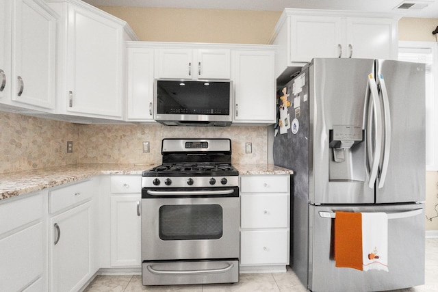 kitchen featuring stainless steel appliances, white cabinetry, backsplash, and light stone countertops