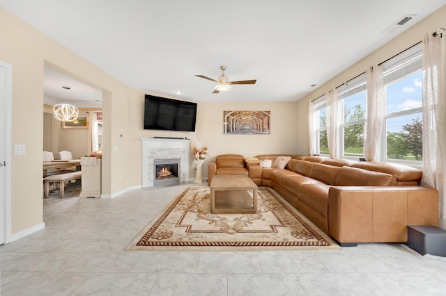 living room featuring a fireplace with flush hearth, ceiling fan, light marble finish flooring, and baseboards