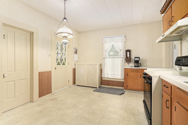 kitchen with range, wallpapered walls, brown cabinetry, light countertops, and hanging light fixtures