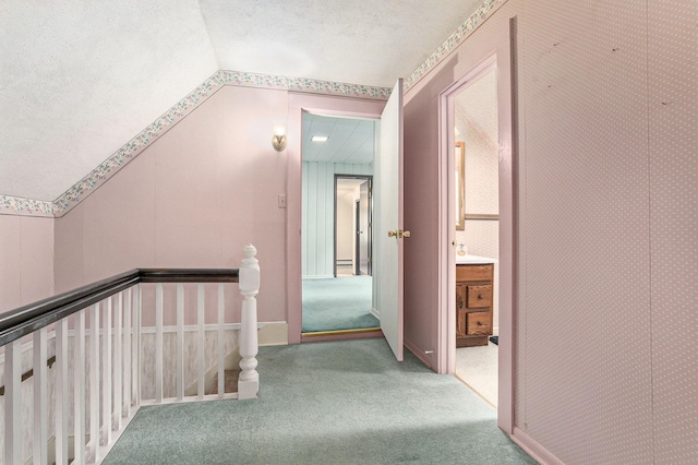 corridor featuring an upstairs landing, carpet flooring, vaulted ceiling, and a textured ceiling