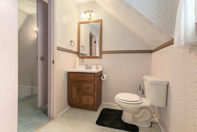 bathroom with toilet, vanity, vaulted ceiling, and wallpapered walls