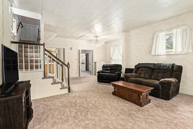 carpeted living room featuring stairs, baseboards, ceiling fan, and crown molding