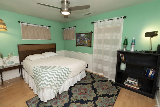 bedroom with wood finished floors, a ceiling fan, and wainscoting