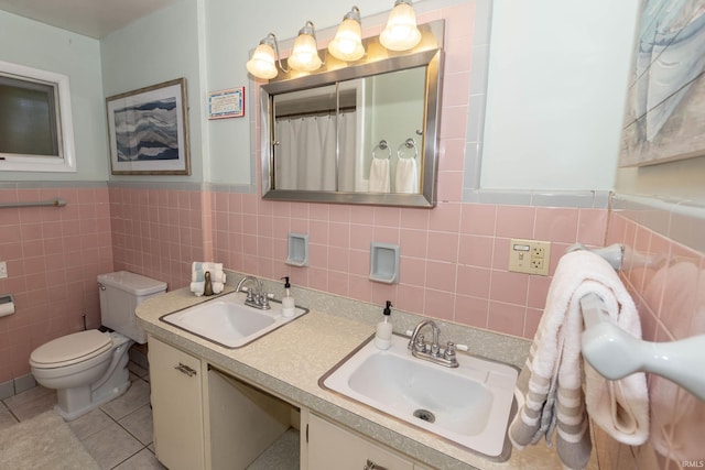 bathroom featuring tile walls, toilet, a wainscoted wall, tile patterned flooring, and double vanity
