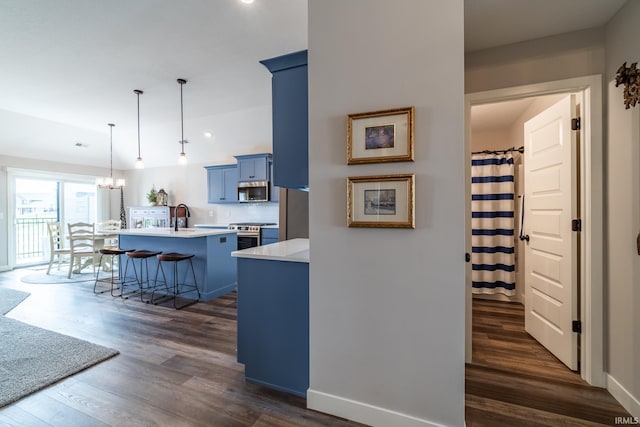kitchen with blue cabinetry, light countertops, dark wood-type flooring, a chandelier, and a kitchen island with sink