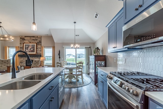 kitchen with appliances with stainless steel finishes, a sink, blue cabinets, a chandelier, and dark wood-type flooring
