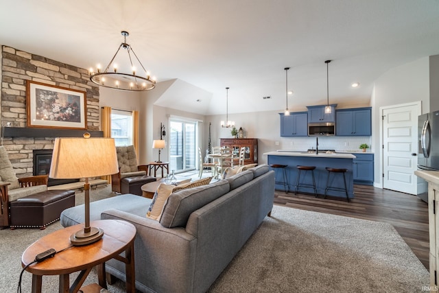 living room with a chandelier, dark wood-style floors, lofted ceiling, a stone fireplace, and recessed lighting