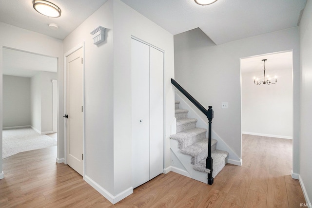 stairway featuring wood finished floors, baseboards, and a chandelier