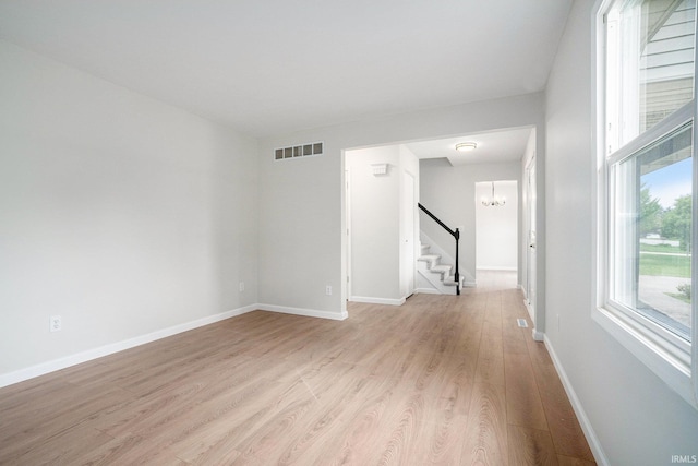 unfurnished room featuring stairway, a chandelier, light wood-style flooring, and baseboards