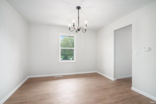 unfurnished room with a chandelier, light wood-style floors, and baseboards