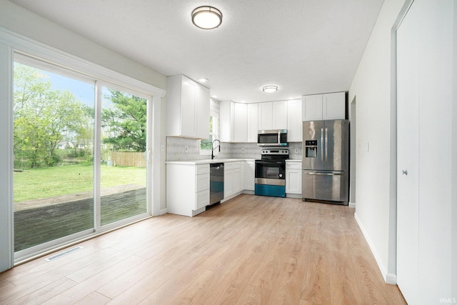kitchen with appliances with stainless steel finishes, light countertops, decorative backsplash, light wood-type flooring, and a sink