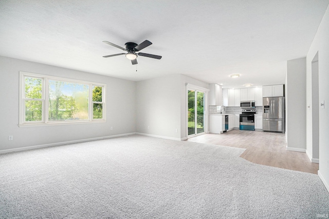 unfurnished living room with light carpet, baseboards, and a ceiling fan