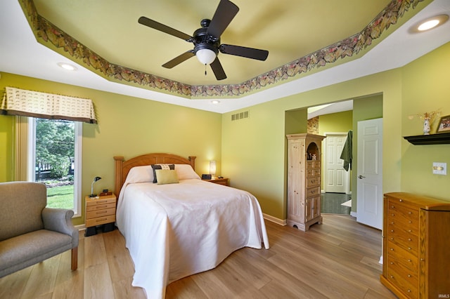 bedroom featuring recessed lighting, light wood-style flooring, baseboards, a tray ceiling, and a ceiling fan
