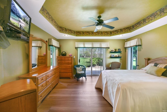 bedroom with access to exterior, wood finished floors, and a raised ceiling