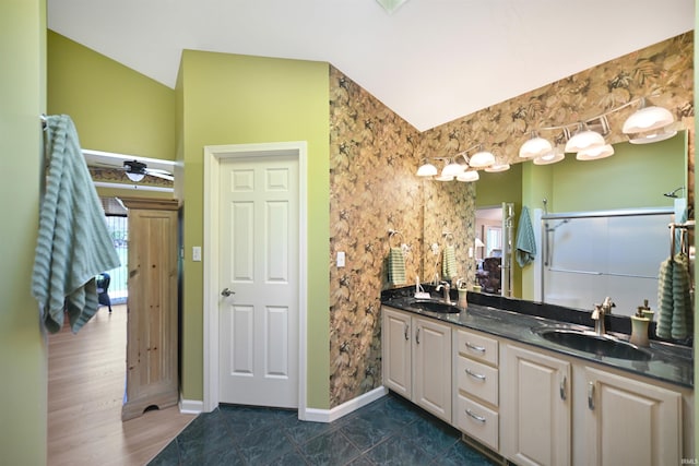 bathroom with lofted ceiling, double vanity, a shower with shower door, and baseboards