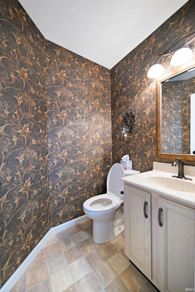 half bath featuring baseboards, wallpapered walls, toilet, and vanity