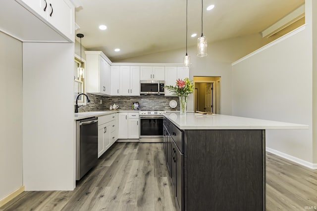 kitchen featuring appliances with stainless steel finishes, a sink, lofted ceiling, tasteful backsplash, and light countertops