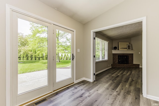 doorway with vaulted ceiling, wood finished floors, baseboards, and a brick fireplace
