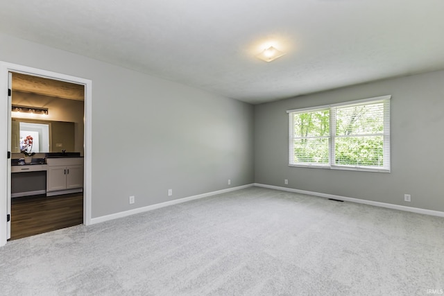 carpeted spare room featuring baseboards and a sink
