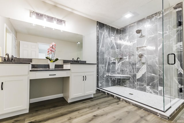 full bathroom with a stall shower, double vanity, and wood finished floors