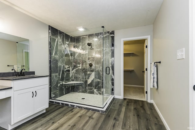 bathroom with a stall shower, wood finished floors, vanity, a walk in closet, and baseboards