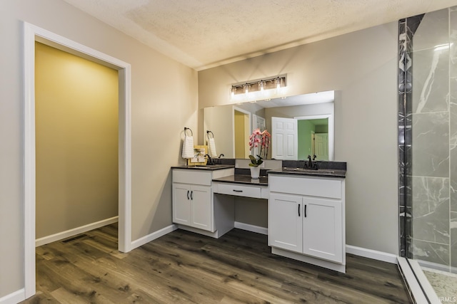 full bathroom with double vanity, wood finished floors, baseboards, and a textured ceiling