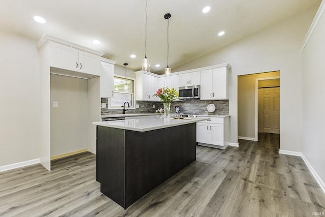 kitchen with stainless steel microwave, backsplash, white cabinets, light wood-style floors, and vaulted ceiling