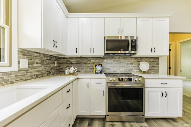 kitchen with stainless steel appliances, light wood-style flooring, white cabinetry, decorative backsplash, and lofted ceiling