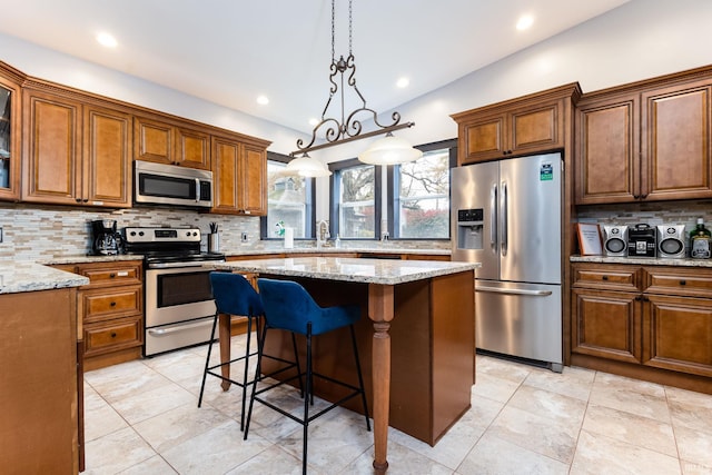 1026 N Michigan St, South Bend, IN 46617 - kitchen featuring appliances with stainless steel finishes, decorative backsplash, brown cabinets, a kitchen island, and light stone countertops