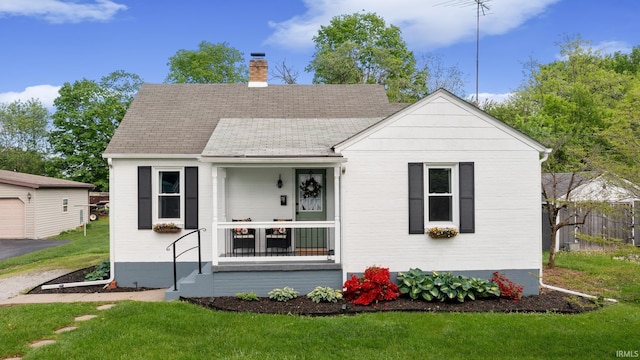 view of front of property with a chimney, a front yard, covered porch, roof with shingles, and an outbuilding