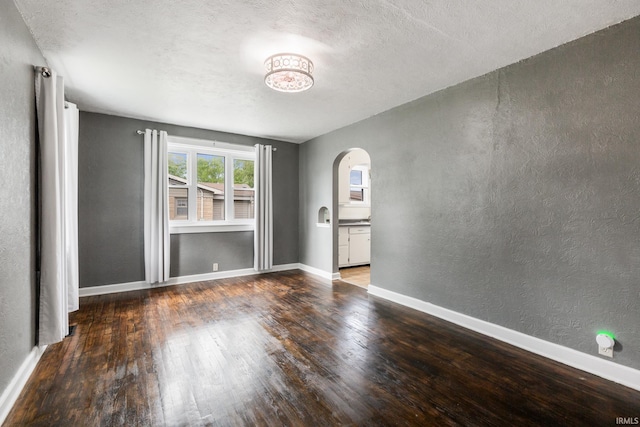 unfurnished room featuring arched walkways, wood finished floors, a textured ceiling, a textured wall, and baseboards